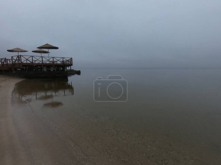 Photo for Sandy beach on calm sea. Calm sea cloudy weather. Smooth waveless sea surface in windless cloudy weather. Calmness. Rainy weather. Pure transparent water. Shoreline coast sea line. Natural background - Royalty Free Image
