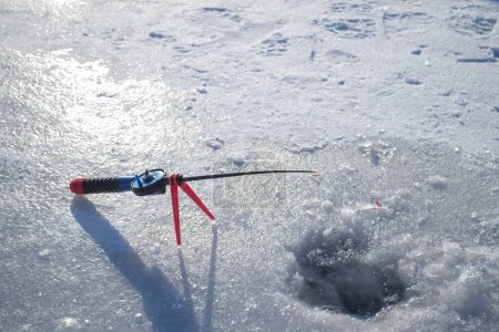 Winter ice fishing. Ice fishing in the winter. Small fishing rod stands near a hole in the ice of a river on a sunny day. Winter activity