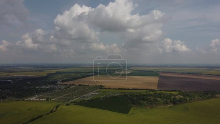 Photo for Fast moving of white clouds in sky above agrarian field of blooming sunflowers and different green agroindustrial fields, brown plowed field, field of ripe wheat on summer sunny day. Aerial drone view - Royalty Free Image