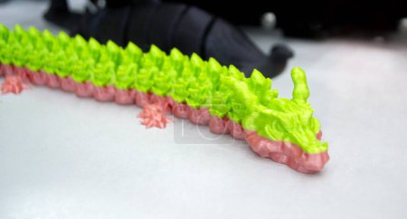 Téléchargez les photos : Prototype de dragon vert rose imprimé en 3D à partir de plastique fondu. Modèle en gros plan de jouet créé sur imprimante 3D. Nouvelle innovation technologies modernes d'impression 3D. Technologie additive progressive. Modèle 3D - en image libre de droit
