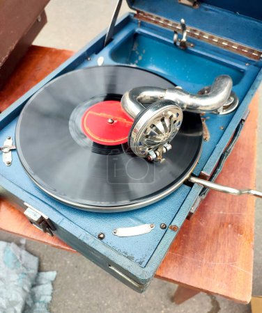 An old retro record playing on old vintage gramophone at flea market. Work of portable gramophone. Old vintage shabby record player, phonograph, potefone. Needle. Nostalgia antique audio turntable