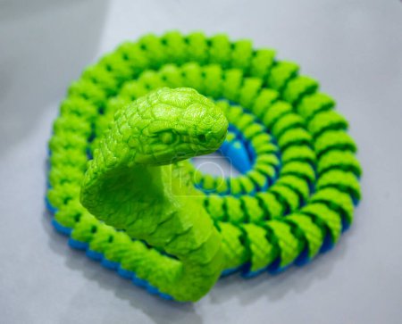 Green snake toy model printed on a 3D printer from melted plastic. Snake-shaped object created by 3D printer. Detailed green prototype printed on 3D printer close-up. New modern additive technologies