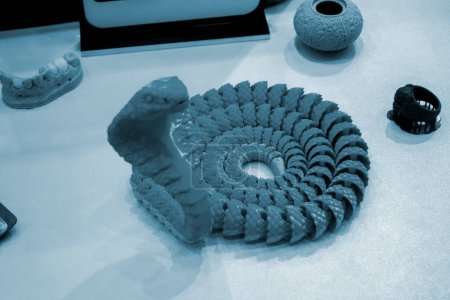Snake toy model printed on a 3D printer from melted plastic. Snake-shaped object created by 3D printer. Detailed green prototype printed on 3D printer close-up. New modern additive technologies