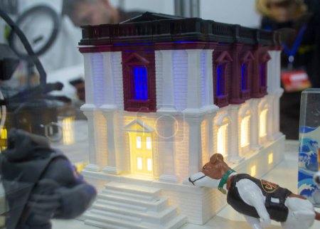 Prototype printed on 3D printer brick building with columns and glowing windows. Model of building with white and brown color, windows with light shining, created by 3D printer from molten plastic