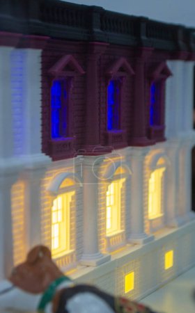 Prototype printed on 3D printer brick building with columns and glowing windows. Model of building with white and brown color, windows with light shining, created by 3D printer from molten plastic