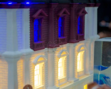 Prototyp gedruckt auf 3D-Drucker Backsteingebäude mit Säulen und glühenden Fenstern. Modell des Gebäudes mit weißer und brauner Farbe, Fenster mit hellem Licht, hergestellt im 3D-Drucker aus geschmolzenem Kunststoff