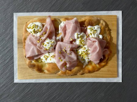 Roman pinsa, variant of the classic Italian pizza topped with mortadella, stracciatella and lamb's lettuce and pistachio