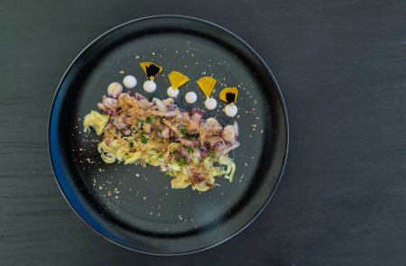 Italian appetizer with octopus and artichokes and sprinkle of bottarga on a black plate