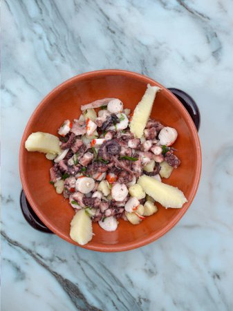Octopus appetizer with potatoes and capers in terracotta dish