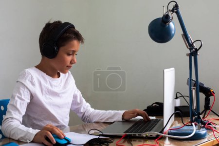 Foto de Niño adolescente feliz sentado en auriculares en la computadora en casa. Niños y aparatos - Imagen libre de derechos