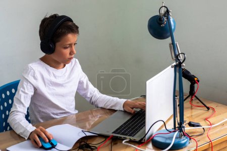 Foto de Niño adolescente atento se sienta en los auriculares en una computadora en casa. Niños y aparatos - Imagen libre de derechos