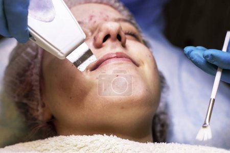 Téléchargez les photos : Heureuse fille tenager au rendez-vous avec un cosmétologue pour le nettoyage du visage au laser - en image libre de droit