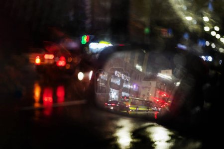Téléchargez les photos : Abstrait fond flou de gouttes de pluie floues sur le miroir gauche d'un embouteillage de voiture dans la ville. Mauvais temps - en image libre de droit