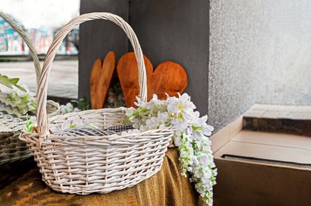 Photo for Cute decorative white wicker basket with white flowers and a wooden heart. Festive mood - Royalty Free Image