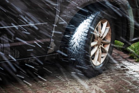 Téléchargez les photos : Roue de voiture dans les pneus d'hiver par mauvais temps avec de la neige lorsque l'herbe devient verte - en image libre de droit