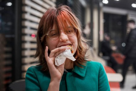 Téléchargez les photos : Élégant teneyger fille avec des cheveux rose vif et des lunettes mange un hamburger - en image libre de droit
