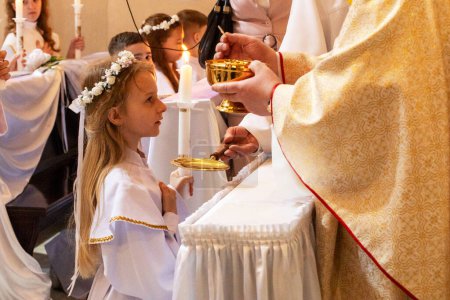 girl in an alba with a burning candle takes the first communion. first communion