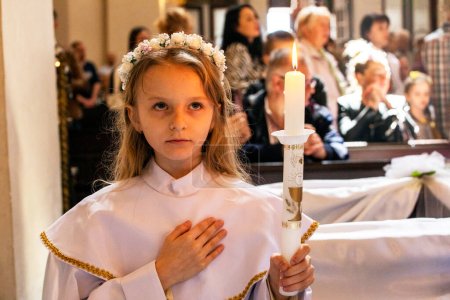 girl in an alba with a burning candle after the first communion. first communion