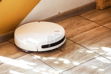 Foto de Aspiradora robot limpia el suelo de baldosas en la sala de estar cerca de las escaleras, horizontal - Imagen libre de derechos