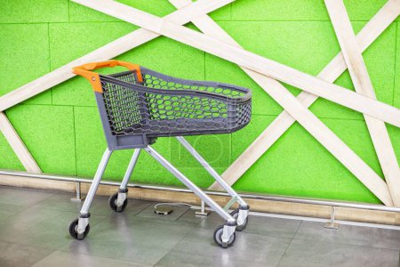 Photo for Shopping empty plastic trolley against the background of a green wall in a shopping center. Shopping for the week - Royalty Free Image