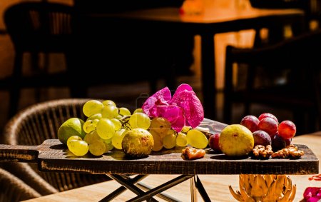 Téléchargez les photos : Fruits verts et raisins bleus, noix et figues sur une planche de bois dans un café à l'extérieur - en image libre de droit