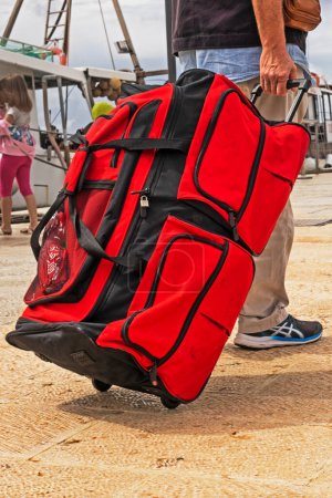 Foto de Llevar una enorme maleta roja, una bolsa sobre ruedas, al muelle hasta el barco. Viajes y ocio - Imagen libre de derechos