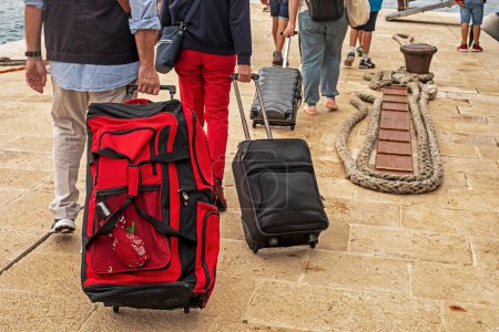 Téléchargez les photos : Les mains des passagers transportent leurs bagages sur des roues sur la jetée par une journée ensoleillée pour monter à bord du paquebot. Voyages et loisirs - en image libre de droit
