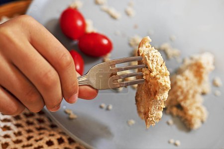 Photo for Child's hand holds a fork with a piece of bitten meat over a gray plate with tomatoes and leftover porridge. Family dinner - Royalty Free Image