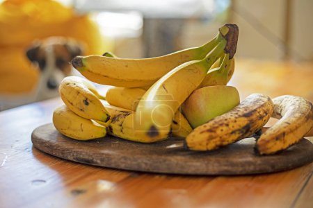 Photo for Branch of bananas lies on a dish on a wooden table in the living room - Royalty Free Image