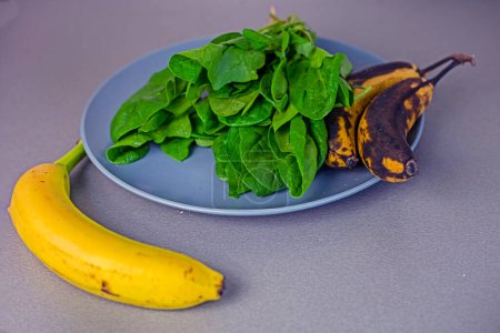 Téléchargez les photos : Banane se trouve sur le comptoir à côté d'une assiette d'épinards et deux bananes trop mûres - en image libre de droit
