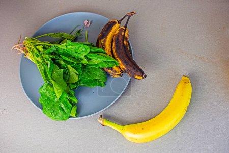 Téléchargez les photos : Banane se trouve sur le comptoir à côté d'une assiette d'épinards et deux bananes trop mûres - en image libre de droit