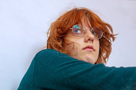 Foto de Retrato de una adolescente con el pelo rojo con gafas mirando hacia un lado. Psicología y complejos de adolescentes - Imagen libre de derechos