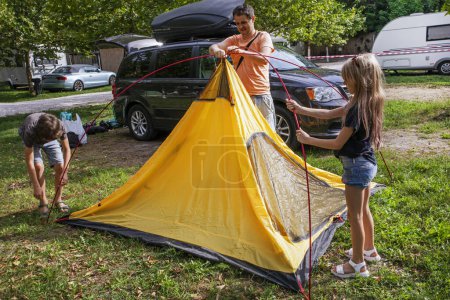 Foto de Papá y los niños instalaron una tienda de campaña en un campamento. Vacaciones familiares y viajes en coche - Imagen libre de derechos