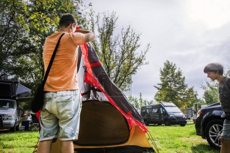 Foto de Papá y su hijo felices cubren una tienda con un toldo en un campamento antes de la lluvia. Vacaciones familiares y viajes en coche - Imagen libre de derechos