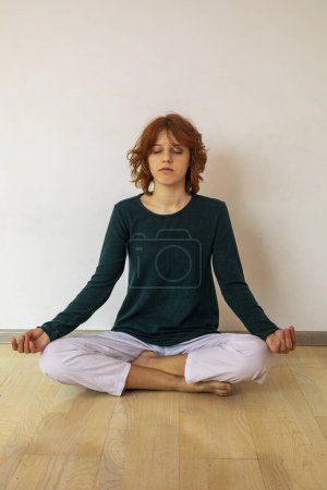 Foto de Feliz chica adolescente con estilo con el pelo de anime rojo se sienta en la posición de loto y medita. Psicología de la edad y el yoga - Imagen libre de derechos