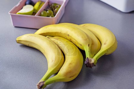 Photo for Bunch of bananas and a row of small containers with snacks. Back to school - Royalty Free Image