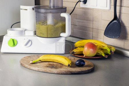 Foto de Machacar plátanos y manzanas y ciruelas en un procesador de alimentos en la cocina - Imagen libre de derechos