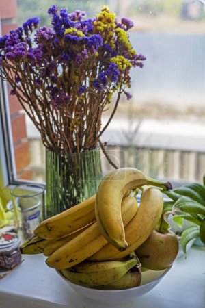 Photo for Plate with bananas next to flowers on the windowsill near the window - Royalty Free Image