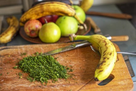 Téléchargez les photos : Bouquet de bananes dans une assiette dans la cuisine près d'une planche à découper avec des herbes - en image libre de droit