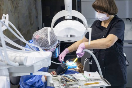 dentist and an assistant in gloves treat a teenager's sore teeth. Dental care and health