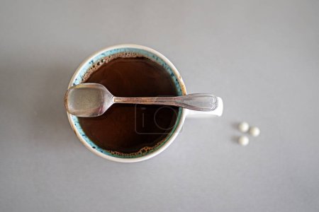 cup with hot natural chocolate and a teaspoon on a gray table and dietary supplements, top view. diabetes