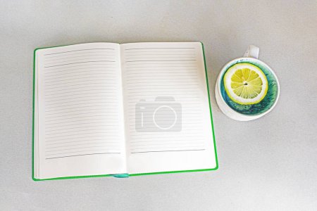 Foto de Planificador semanal abierto en la mesa junto a una taza de limón. Buenos días, empanado del día, semana, mes, año - Imagen libre de derechos