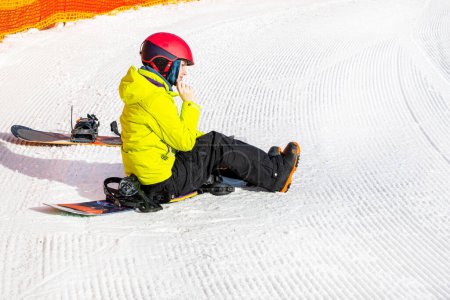 Snowboarder sitzt auf einem Snowboard auf nassem, losem Schnee vor dem Skifahren. Aktive Erholung