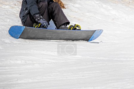 Snowboarder sitzt auf einem Snowboard auf nassem, losem Schnee vor dem Skifahren. Aktive Erholung