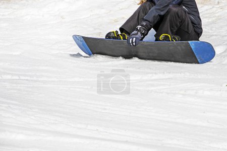 snowboarder se sienta en una tabla de snowboard sobre nieve mojada y suelta antes de esquiar. recreación activa