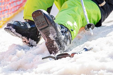 Skifahrer schnürt Skischuhe auf schneebedeckter Piste. Aktivurlaub mit der Familie