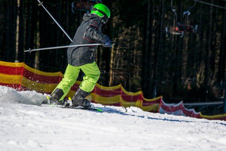 Skifahrerjunge mit grünem Helm steigt im Carving-Stil vom Berg ab. Aktive Familienfreizeit