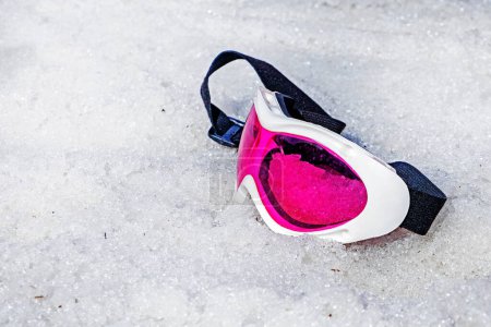 máscara de mentira rosa se encuentra en una pendiente húmeda y nevada en un día soleado. Temporada de nieve de invierno. Vacaciones activas con la familia