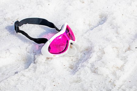 Die rosafarbene Kindergesichtsmaske liegt an einem sonnigen Tag auf einem nassen, schneebedeckten Hang. Winterzeit. Aktivurlaub mit der Familie