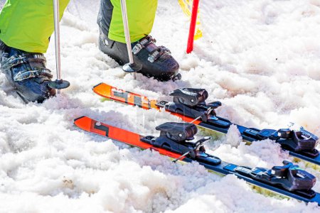 Skifahrer schnürt an einem sonnigen Tag seine Skischuhe an einem verschneiten Hang. Aktiver Familienurlaub